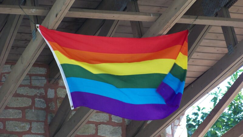 A rainbow flag waving on a porch.