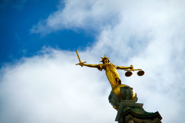 A golden statue holding the scales of justice in one hand and a sword in the other against a blue sky backdrop.