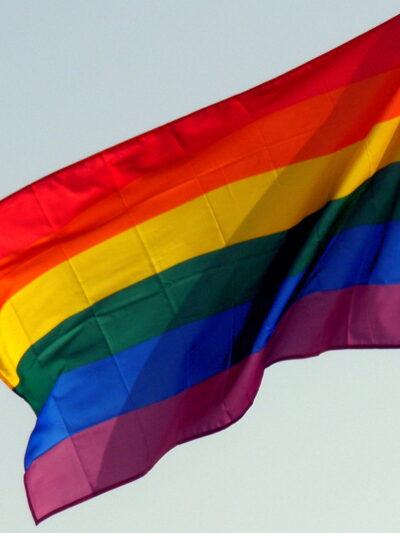 A rainbow flag against the backdrop of a blue sky.