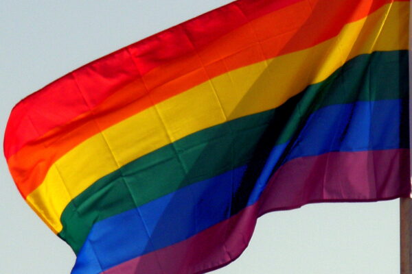 A rainbow flag against the backdrop of a blue sky.