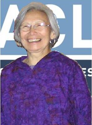A picture of Joan Hamilton, an elderly Alaska Native woman, standing against an ACLU banner.