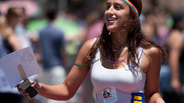A woman wearing a Pride headband and many signs marches in a parade.
