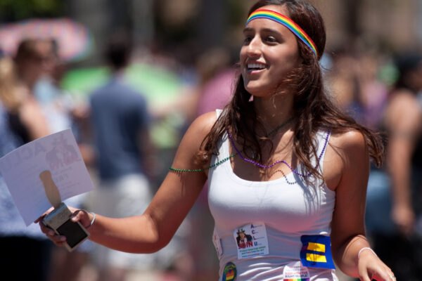 A woman wearing a Pride headband and many signs marches in a parade.