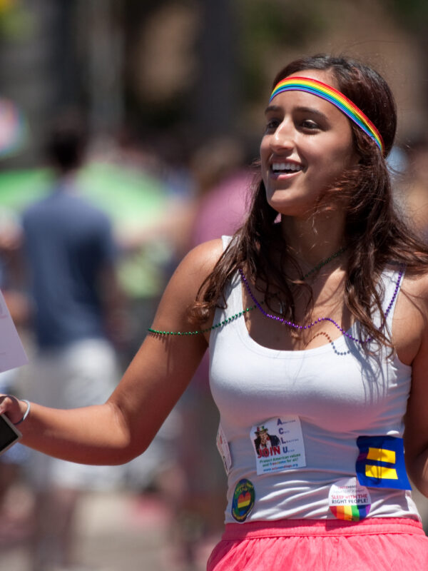 A woman wearing a Pride headband and many signs marches in a parade.