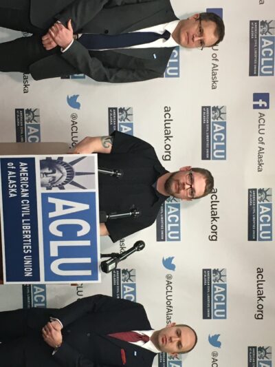 ACLU staff attorney Eric Glatt, plaintiff Lance Hunt, and executive director Joshua Decker stand in front of a podium