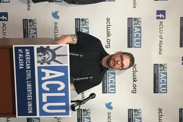 ACLU staff attorney Eric Glatt, plaintiff Lance Hunt, and executive director Joshua Decker stand in front of a podium