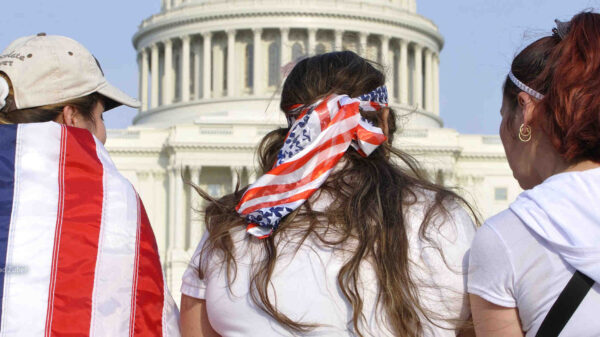 Three women in front of the Capitol, two draped in American flags.