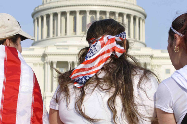 Three women in front of the Capitol, two draped in American flags.