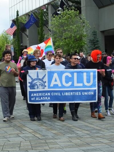 A group of people marching behind the ACLU banner.