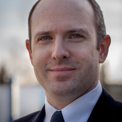 Executive Director Joshua Decker stands against a blue sky backdrop wearing an ACLU lapel pin.