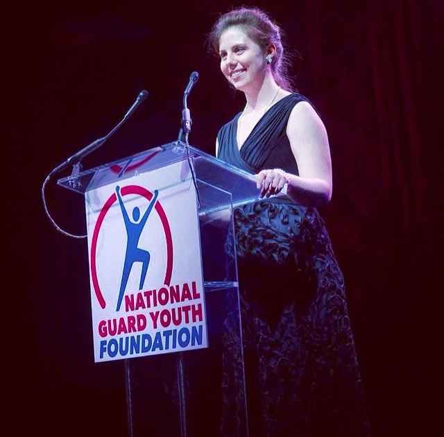 A young woman speaks on a stage from behind a podium.