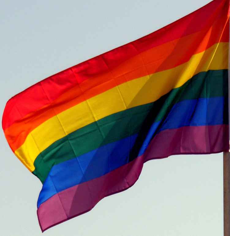 A rainbow flag against the backdrop of a blue sky.