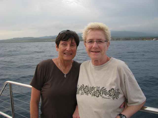 Two women stand on a boat out at sea.