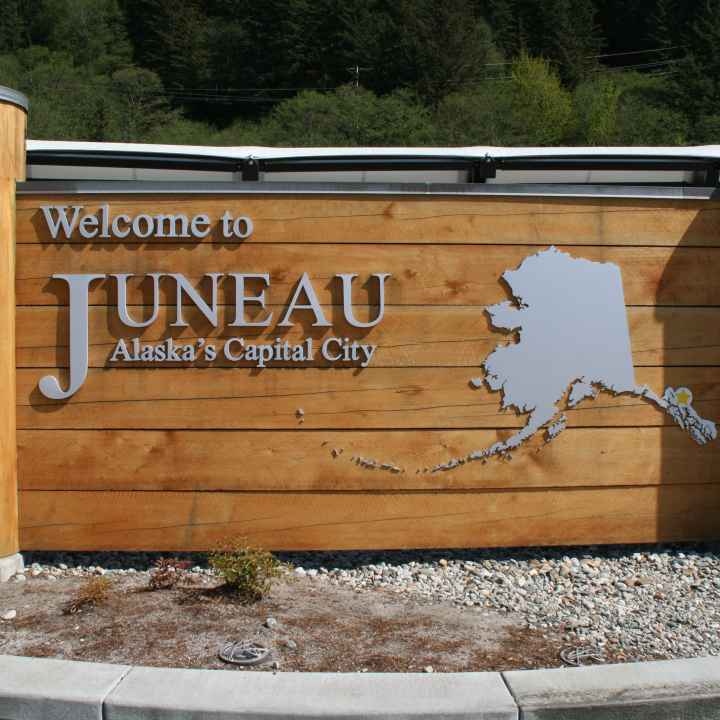 A wooden sign says &quot;Welcome to Juneau - Alaska&#039;s Capital City&quot; next to a map of Alaska