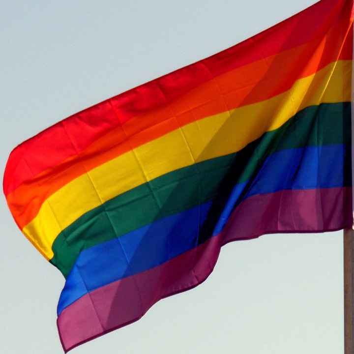 A rainbow flag against the backdrop of a blue sky.