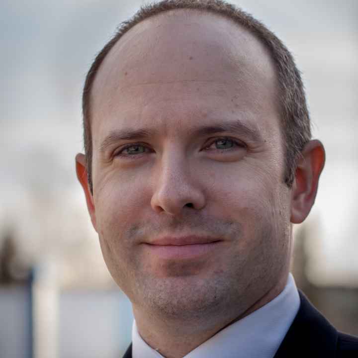 Executive Director Joshua Decker stands against a blue sky backdrop wearing an ACLU lapel pin.