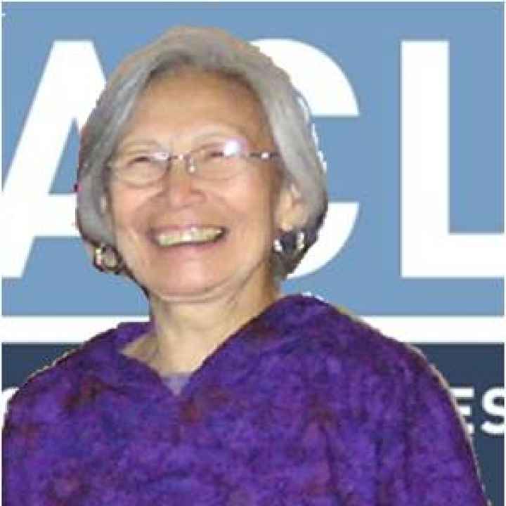 A picture of Joan Hamilton, an elderly Alaska Native woman, standing against an ACLU banner.