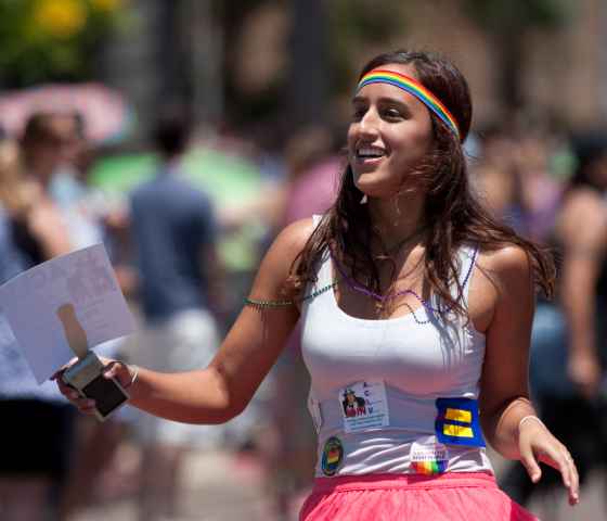 A woman wearing a Pride headband and many signs marches in a parade.